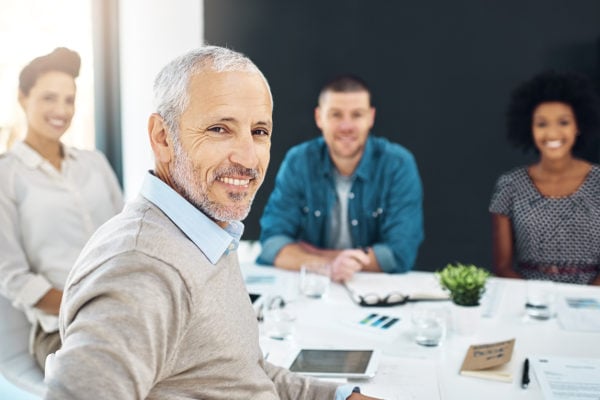 A team of educational consultants around a conference table, the consultant nearest the camera turned to smile.