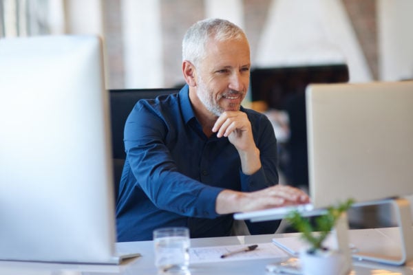 An independent educational consultant working at his desk between two monitors.
